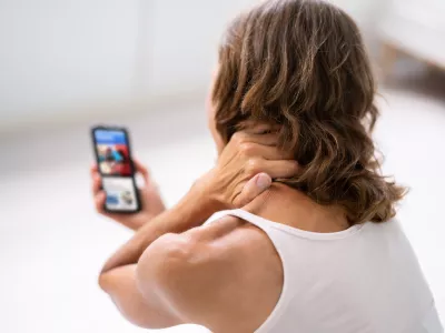 Woman With Neck Pain Sitting Using Mobile Phone
