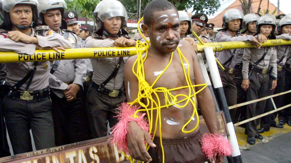 A Papuan protester stands near riot police officers during a demonstration in Surabaya, East Java, Indonesia, Wednesday, March 22, 2006, demanding that U.S. mining giant Freeport close its massive gold mine in Papua province. Indonesia is sending hundreds more police troops to the province to prevent further unrest as the number of security officers killed in protests there last week rose to five. (AP Photo/Trisnadi)
