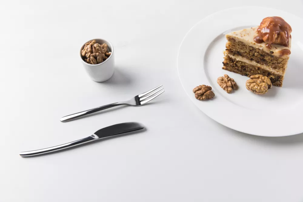 Cutlery and plate with cake placed on white surface / Foto: Lightfieldstudios