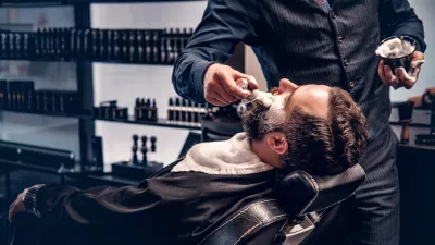Barber applies shaving foam to a man's face in a saloon. / Foto: Fxquadro