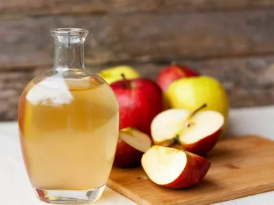 Apple organic vinegar in glass pitcher and ripe fresh red and yellow apples wooden background. Healthy organic food concept.
