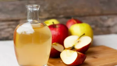 Apple organic vinegar in glass pitcher and ripe fresh red and yellow apples wooden background. Healthy organic food concept.