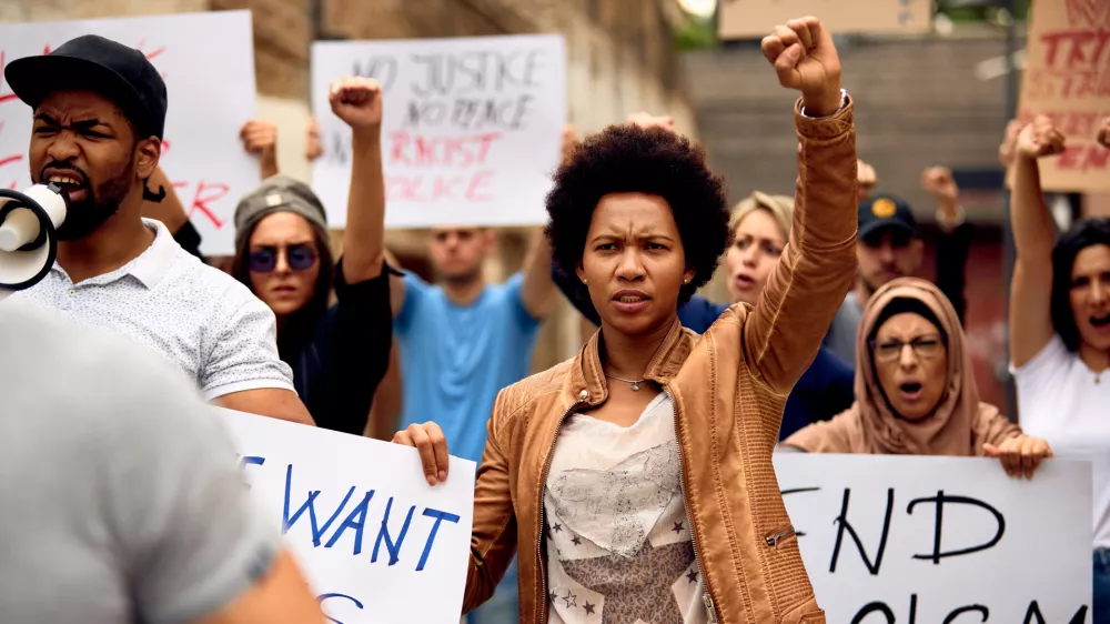 Multi-ethnic crowd of people protesting against racism on city streets. Focus is on African American woman with raised fist. / Foto: Drazen Zigic
