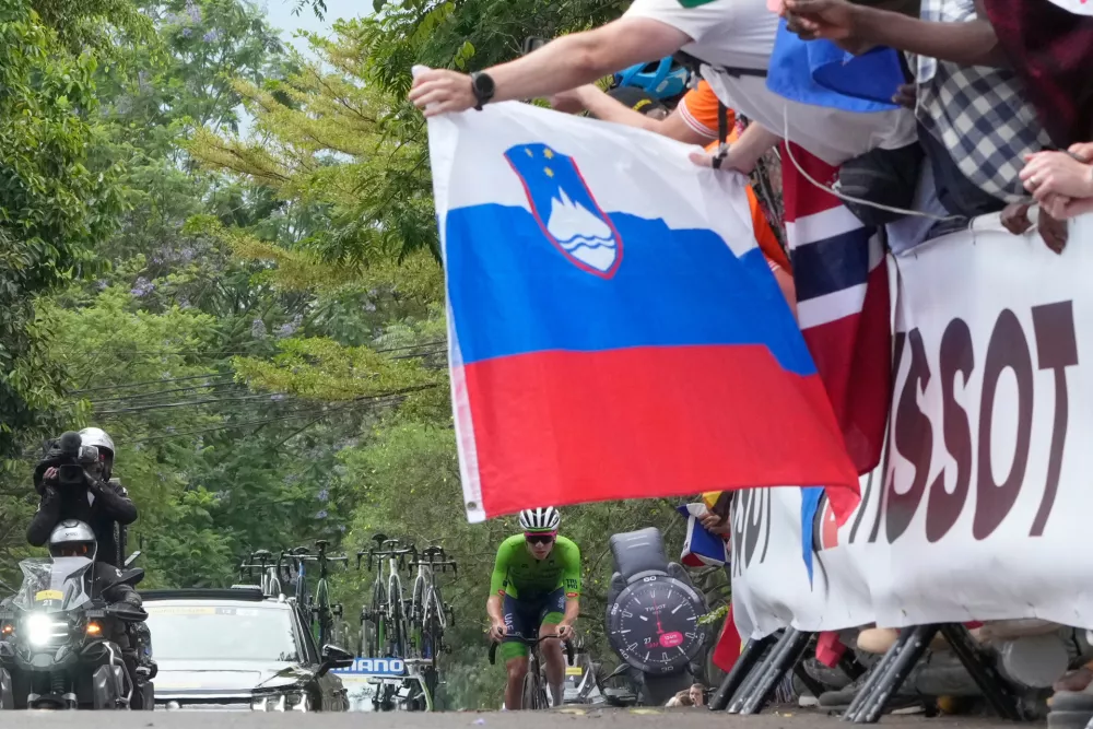 Slovenia's Tadej Pogacar is framed by a Slovenian flag as he leads the men's Elite road race, at the road cycling World Championships in Kigali, Rwanda, Sunday, Sept. 28, 2025. (AP Photo/Jerome Delay)