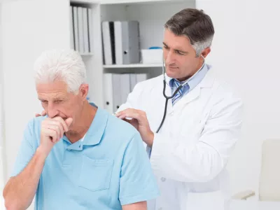 ﻿Male doctor examining coughing senior patient in clinic
