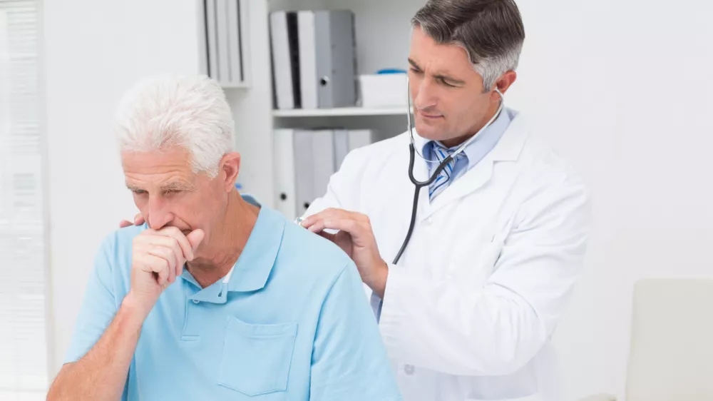 ﻿Male doctor examining coughing senior patient in clinic