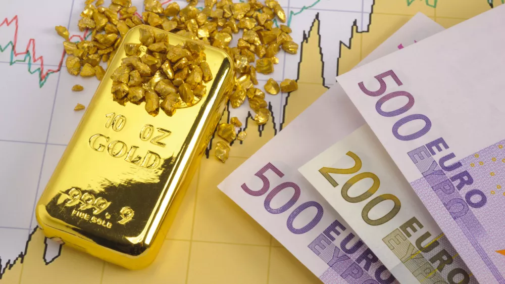 gold bar and European currency laying on chart of stock market