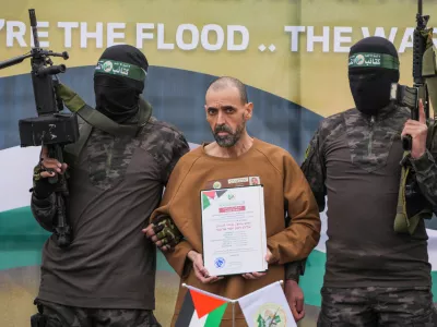 FILE - Israeli captive, Eli Sharabi, who has been held hostage by Hamas in Gaza since October 7, 2023, stands on a stage escorted by Hamas fighters before being handed over to the Red Cross in Deir al-Balah, central Gaza Strip, Saturday Feb. 8, 2025. (AP Photo/Abdel Kareem Hana, File)