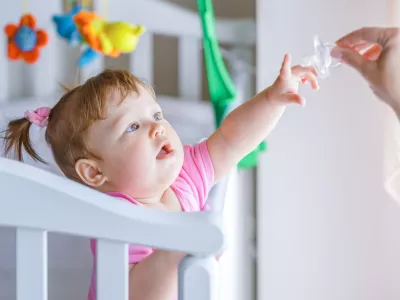 ﻿Little girl pulls her hand to the dummy, standing in a baby crib