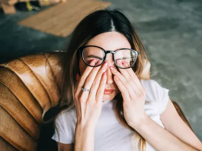 Young woman rubs her eyes after using glasses. Eye pain or fatigue concept. / Foto: Nikkimeel