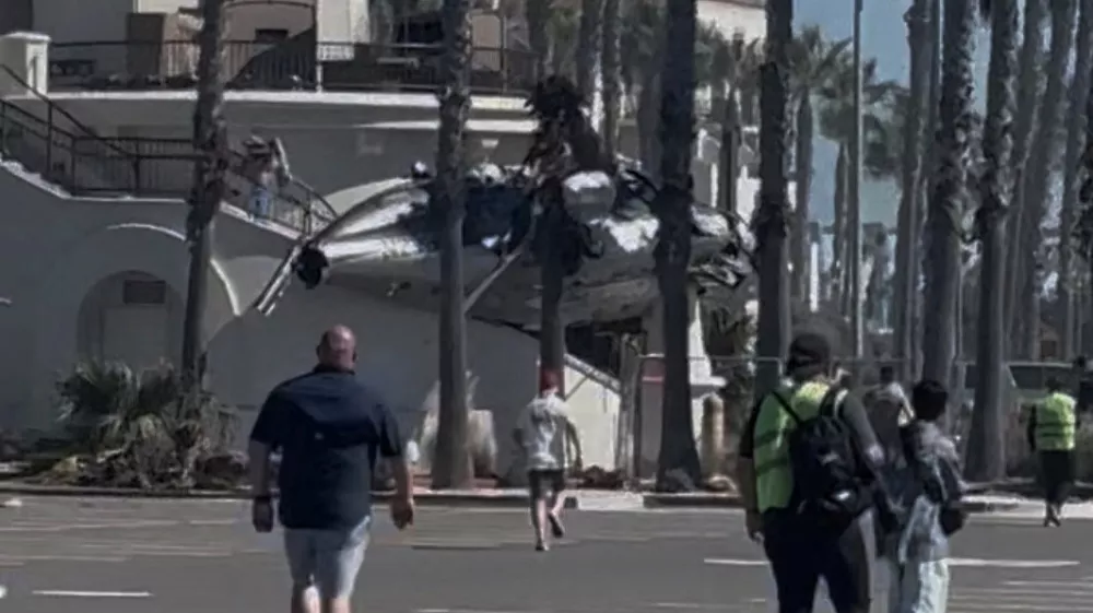People and emergency personnel walk next to a helicopter wreckage lying on a structure following a crash in Huntington Beach, California, U.S., October 11, 2025, in this screengrab obtained from social media video. Tim Robinson/via REUTERS THIS IMAGE HAS BEEN SUPPLIED BY A THIRD PARTY. MANDATORY CREDIT. NO RESALES. NO ARCHIVES. VERIFICATION - Reuters was able to independently verify the location of the video by building exterior, structures and trees matched file images. - Reuters was able to verify the date of the footage from the original file metadata.