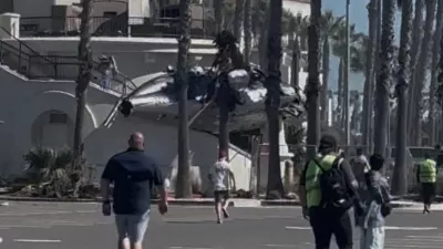 People and emergency personnel walk next to a helicopter wreckage lying on a structure following a crash in Huntington Beach, California, U.S., October 11, 2025, in this screengrab obtained from social media video. Tim Robinson/via REUTERS THIS IMAGE HAS BEEN SUPPLIED BY A THIRD PARTY. MANDATORY CREDIT. NO RESALES. NO ARCHIVES. VERIFICATION - Reuters was able to independently verify the location of the video by building exterior, structures and trees matched file images. - Reuters was able to verify the date of the footage from the original file metadata.