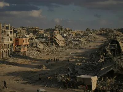 Palestinians walk among destroyed buildings in Gaza City, Sunday, Oct. 12, 2025, after Israel and Hamas agreed to a pause in their war and the release of the remaining hostages. (AP Photo/Jehad Alshrafi)