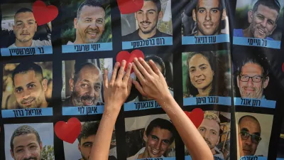 A person pastes a heart-shaped sticker on a banner with pictures of Israeli hostages during a a gathering at a plaza known as hostages square in Tel Aviv, Israel, Monday, Oct. 13, 2025. (AP Photo/Oded Balilty)