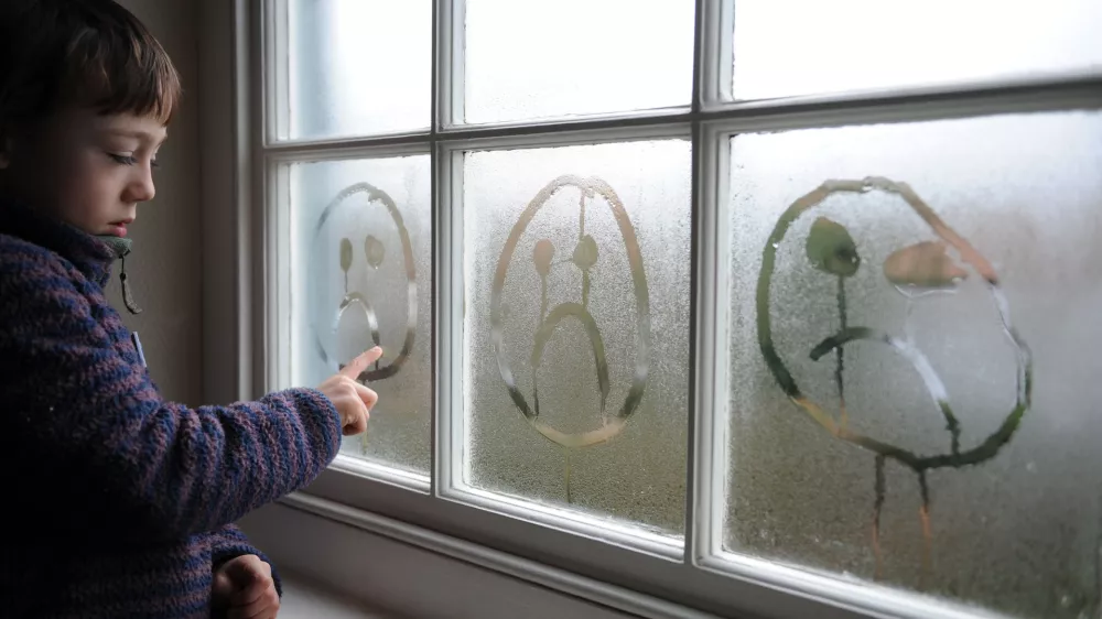 D1YK37 8 year old drawing a sad face in the condensation on a window.