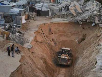 Palestinians watch members of the Hamas militant group searching for bodies of the hostages in Khan Younis, southern Gaza Strip, Saturday, Oct. 18, 2025. (AP Photo/Jehad Alshrafi)