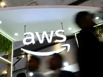 FILE PHOTO: People walk past the logo of Amazon Web Services (AWS) at its exhibitor stall at the India Mobile Congress 2025 at Yashobhoomi, a convention and expo center in New Delhi, India, October 8, 2025. REUTERS/Anushree Fadnavis/File Photo