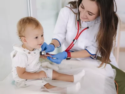 Female doctor checking child's lungs during medical checkup at the medical clinic. Woman pediatrician using stethoscope to examine breathing and heartbeat of young patient.