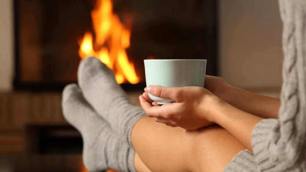 Woman with socks holding coffee in a fireplace / Foto: Antonioguillem