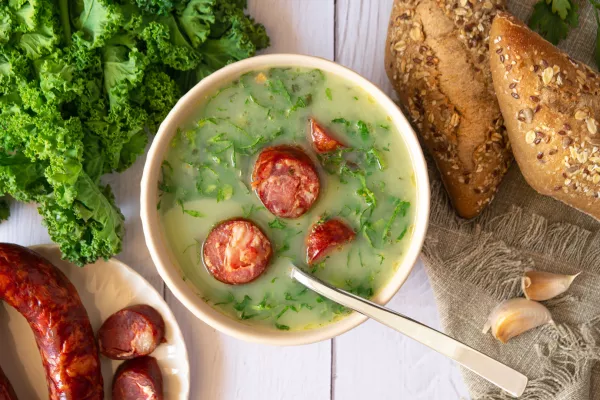 Portuguese style soup called Caldo Verde, bread, Cabbage julienne, and chorizo sausage on a white wooden Table. Flat lay / Foto: Iggi_boo