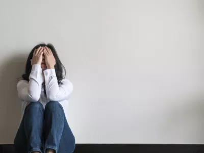 Anxiety disorder menopause woman, stressful depressed emotional person with mental health illness, headache and migraine sitting feeling bad sadly with back against wall on the floor in domestic home / Foto: Chinnapong