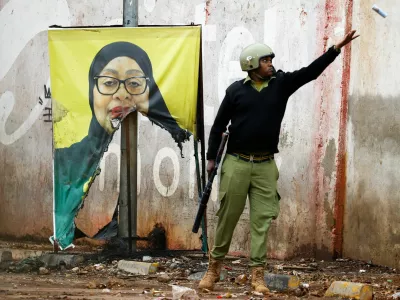 A Tanzanian riot police officer throws a used teargas canister near a vandalised campaign poster of President Samia Suluhu Hassan, following a protest a day after a general election marred by violent demonstrations over the exclusion of two leading opposition candidates at the Namanga One-Post Border crossing point between Kenya and Tanzania, October 30, 2025. REUTERS/Thomas Mukoya