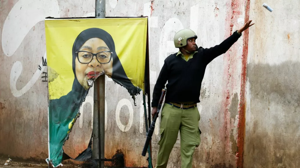 A Tanzanian riot police officer throws a used teargas canister near a vandalised campaign poster of President Samia Suluhu Hassan, following a protest a day after a general election marred by violent demonstrations over the exclusion of two leading opposition candidates at the Namanga One-Post Border crossing point between Kenya and Tanzania, October 30, 2025. REUTERS/Thomas Mukoya