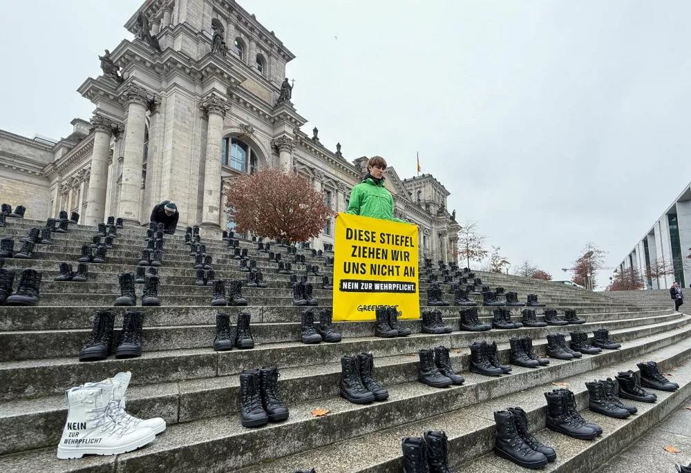 Knob cup army boots sit on the steps next to a banner reading "We are not putting on this boots - No to compulsory military service", during a Greenpeace Youth protest against plans to reintroduce compulsory military service in Germany, in front of the Bundestag, Germany's lower house of parliament, in Berlin, Germany, November 10, 2025. REUTERS/Leon Malherbe