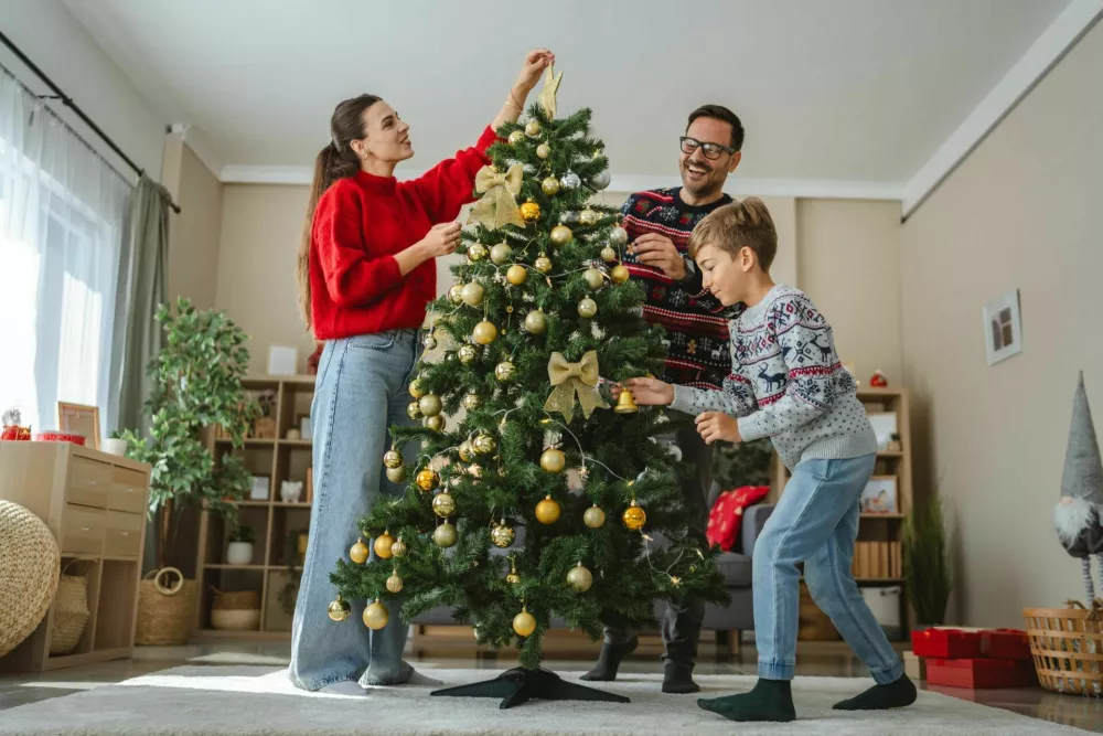Happy family decorating beautiful christmas tree with golden and white ornaments and warm lights, enjoying their time together during winter holidays / Foto: Miljan Živković