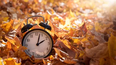 Alarm clock among golden yellow fall leaves with bright sunshine, autumn time change concept