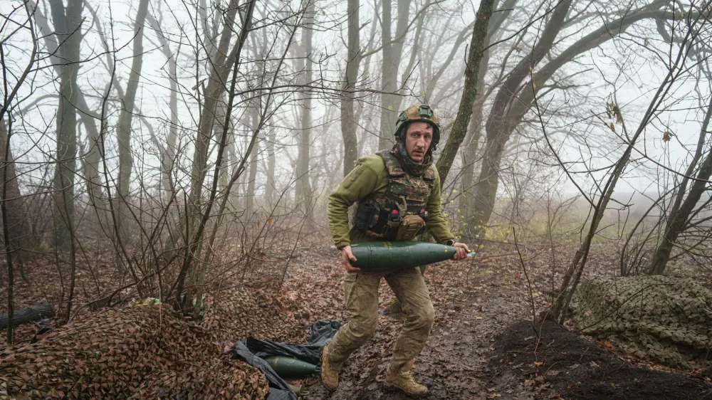 A Ukrainian serviceman of the Da Vinci Wolves Battalion carries an artillery shell before firing toward Russian positions at the front line in eastern Ukraine, on Friday, Nov. 28, 2025. (AP Photo/Evgeniy Maloletka)
