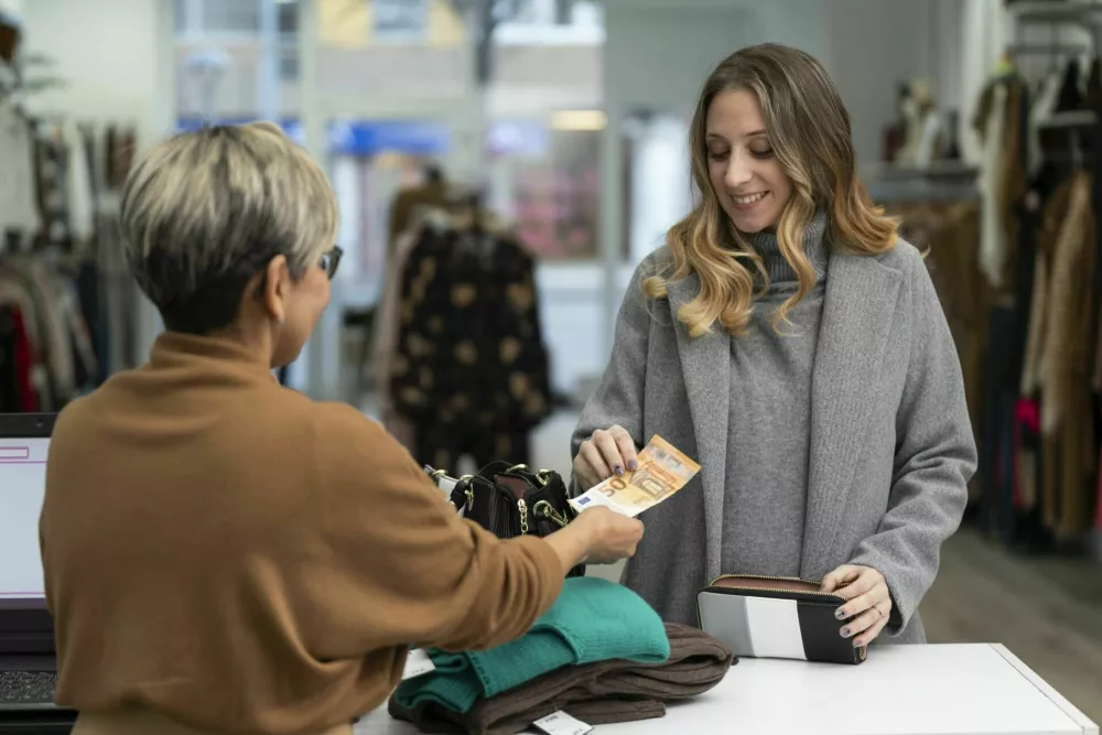 Young blonde woman paying in cash at the clothing store with a fifty euro bill to the clerk / Foto: Marc Calleja Lopez
