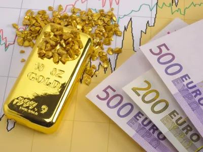 gold bar and European currency laying on chart of stock market