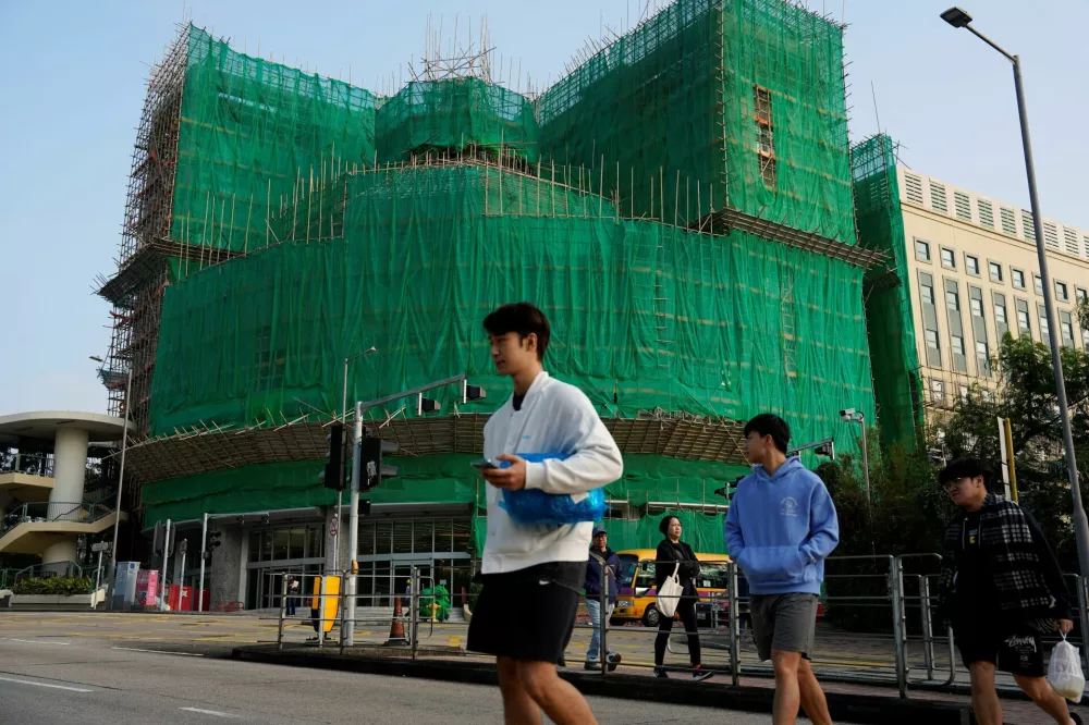 People walk past bamboo scaffolding and mesh outside a building at Hong Kong Baptist University, following authorities' decision to remove the netting amid investigations into a deadly fire at Wang Fuk Court, in Hong Kong, China December 4, 2025. REUTERS/Vernon Yuen
