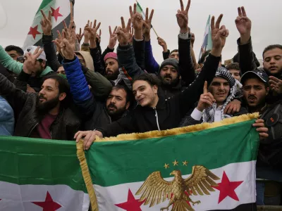 People celebrate and wave Syrian flags as they wait for a parade by the new Syrian army during celebrations marking the first anniversary of the ousting of former President Bashar Assad in Damascus, Syria, Monday, Dec. 8, 2025. (AP Photo/Hussein Malla)