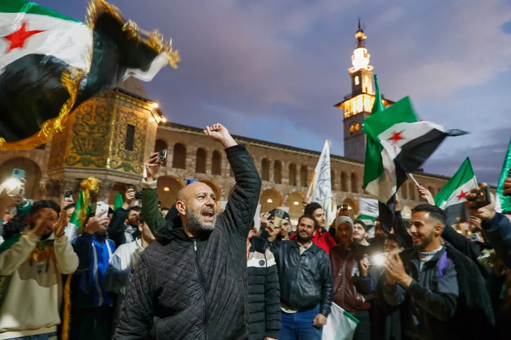 Syrians shout slogans and wave flags outside the Umayyad Mosque before a prayer held ahead of celebrations marking the first anniversary of the ousting of the Bashar Assad regime in Damascus, Syria, Monday, Dec. 8, 2025. (AP Photo/Omar Sanadiki)