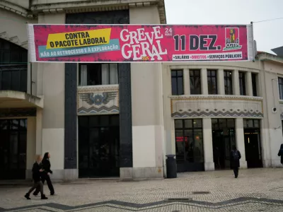 People walk past a banner calling for a general strike during a nationwide walkout to protest a new labour package announced by the centre-right government in Lisbon, Thursday, Dec. 11, 2025. (AP Photo/Armando Franca)