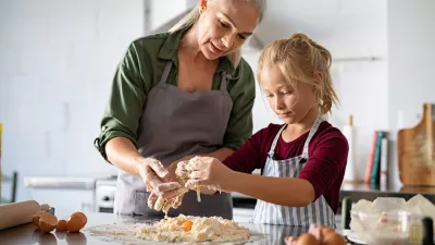 Cute girl learning preparing dough with mature grandmother in kitchen. Lovely old grandma and granddaughter preparing cookies with flour and eggs on kitchen counter. Senior granny in apron teaching her child to make cookies or pie. / Foto: Ridofranz