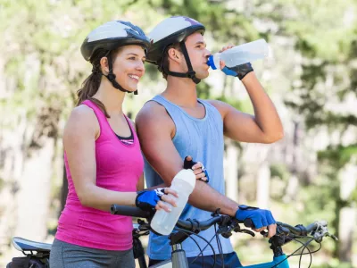 Young couple holding water bottle while riding bicycle at forest / Foto: Wavebreakmedia