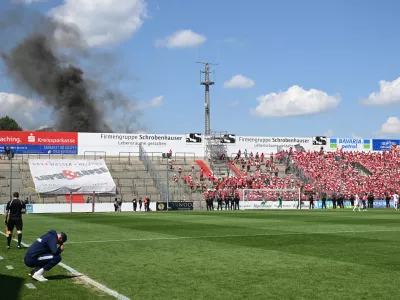 FILED - 11 June 2023, Bavaria, Unterhaching: Unterhaching coach Sandro Wagner (L) sits on the edge of the pitch while thick smoke rises behind the north stand during the the Regionalliga promotion round to the 3rd division soccer match between SpVgg Unterhaching and Energie Cottbus at Sportpark Unterhaching. The Bild paper said the council of the municipality of Unterhaching near Munich has given the green light to sell its 15,000-seat Sportpark Unterhaching stadium to Bayern for &middot;7.25 million (.5 million). Photo: Angelika Warmuth/dpa