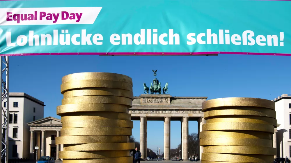 FILED - 07 March 2022, Berlin: Figures of coins pile up under a banner at an Equal Pay Day event in front of the Brandenburg Gate. Photo: Paul Zinken/dpa
