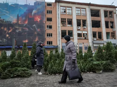 A woman walks past a street market selling Christmas trees, amid Russia's attack on Ukraine, in front of a building damaged by Russian missile and drone strikes in Kyiv, Ukraine December 16, 2025. REUTERS/Gleb Garanich