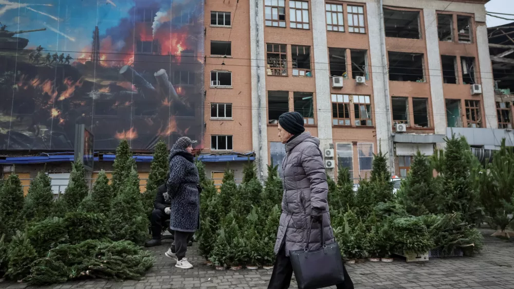 A woman walks past a street market selling Christmas trees, amid Russia's attack on Ukraine, in front of a building damaged by Russian missile and drone strikes in Kyiv, Ukraine December 16, 2025. REUTERS/Gleb Garanich