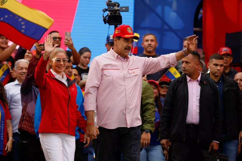 FILE PHOTO: Venezuela's President Nicolas Maduro waves while holding the hand of his wife Cilia Flores during a ceremony to swear in new community-based organisations, as U.S. President Donald Trump's administration ramps up pressure on Maduro's government, in Caracas, Venezuela, December 1, 2025. REUTERS/Leonardo Fernandez Viloria/File Photo