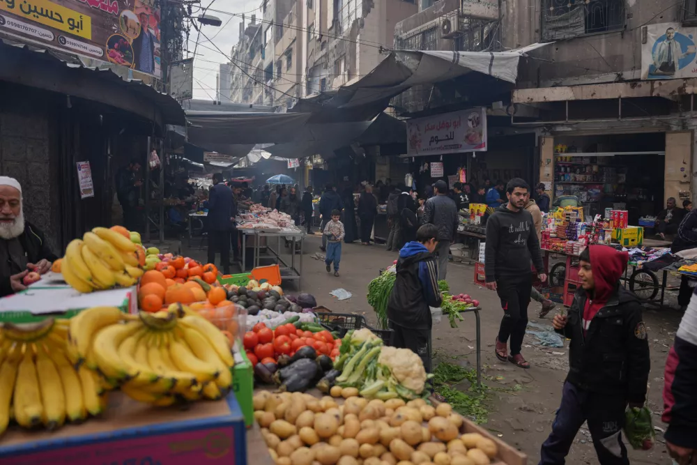 Palestinians walk along street market where fruits and vegetables are displayed for sale in Gaza City, Friday, Dec. 19, 2025. (AP Photo/Abdel Kareem Hana)