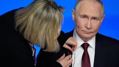 A TV assistant attaches a microphone to Russian President Vladimir Putin's suit prior to his annual news conference and call-in show at Gostinny Dvor, in Moscow, on Friday, Dec. 19, 2025. (AP Photo/Pavel Bednyakov)