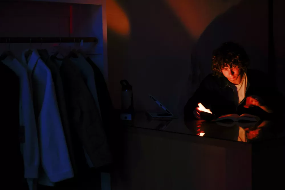 Miles Barrett, assistant designer at Industry of All Nations, reads "Red Rising" by Pierce Brown by candlelight during a power outage in San Francisco, Saturday, Dec. 20, 2025. (Yalonda M. James/San Francisco Chronicle via AP)