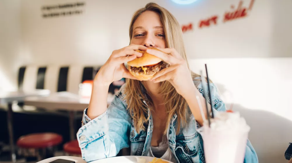 Young woman eating burger in restaurant / Foto: Diem.ph