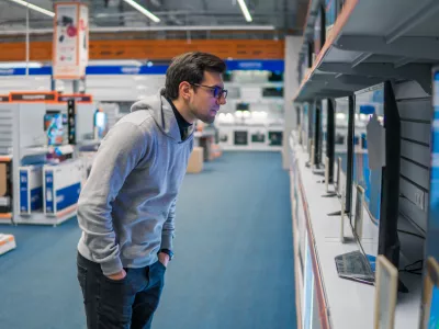 Smart modern male customer examining large TV-sets at electronics store. He looks at new display.. New screen generations.