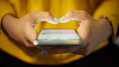 Young woman using cell phone to send text message on social network at night. Closeup of hands with computer laptop in background / Foto: Diego_cervo,getty Images/istockphoto